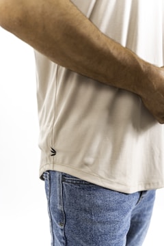 A close-up of a person wearing a beige t-shirt and blue jeans. The focus is on the side waist area, showcasing the texture and fabric details. The image highlights the casual attire.