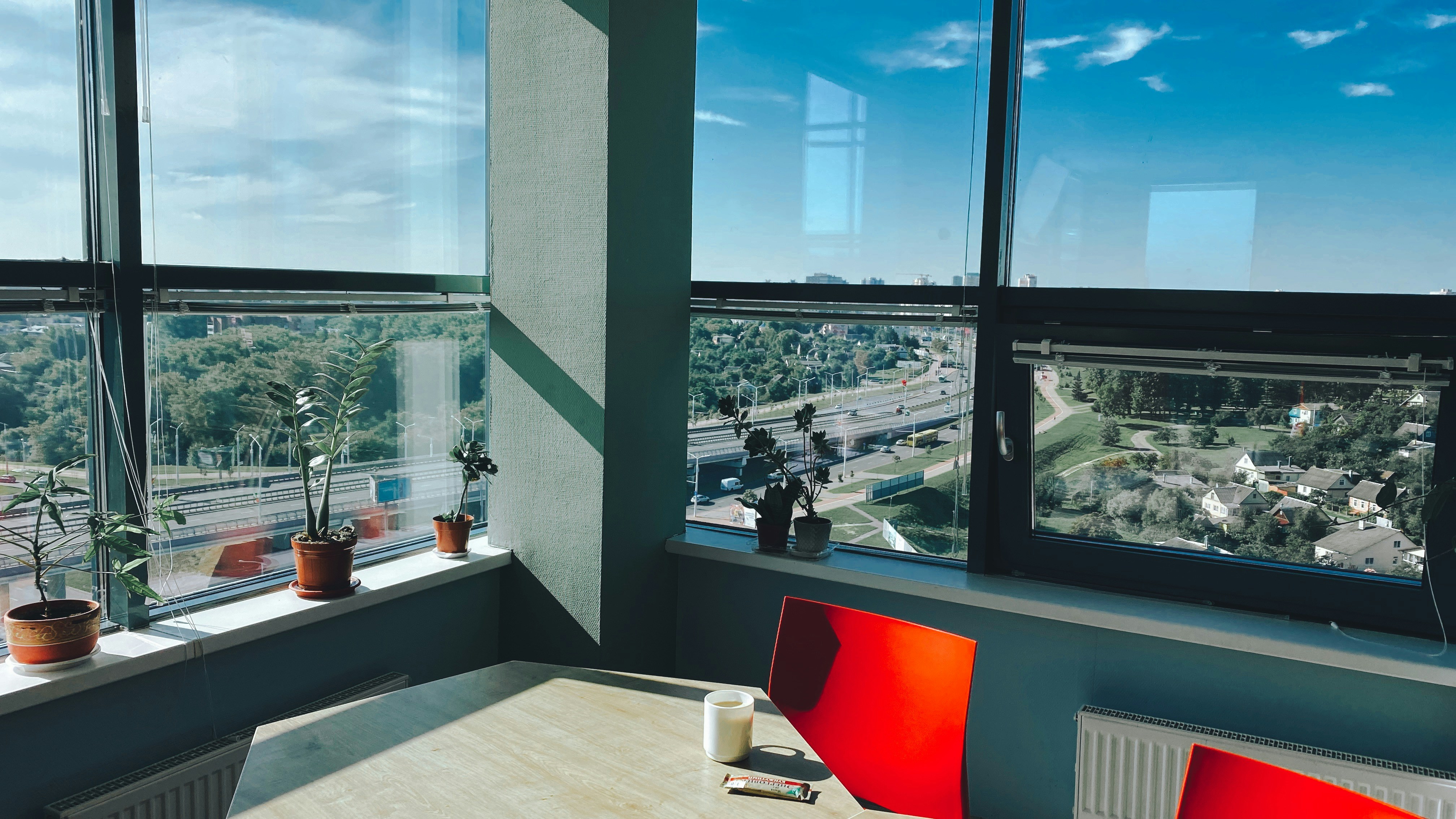 Sunlit office with city view and red chairs.