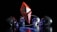 Four metallic skulls surround a glowing red geometric shape resembling an inverted pyramid and an upright pyramid joined at the base. A reflective ring encircles the shapes in a dark, glossy environment, creating a mysterious and futuristic atmosphere.