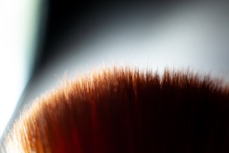 An animated brush applying smooth foundation with a golden glow on a black background with red accents.