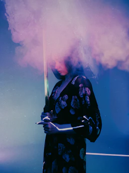 A mysterious figure blindfolded and bound, surrounded by eight swords under a twilight sky.