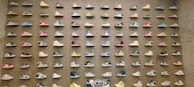 A wall display featuring rows of colorful sneakers, each pair mounted neatly in a uniform grid pattern. The sneakers vary in style and color, with vibrant hues and unique designs creating a visually striking effect.