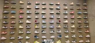 A wall display featuring rows of colorful sneakers, each pair mounted neatly in a uniform grid pattern. The sneakers vary in style and color, with vibrant hues and unique designs creating a visually striking effect.