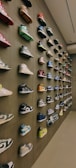 A wall displays a diverse collection of sneakers, arranged neatly in rows. Various colors and styles are represented, with the shoes mounted in an aesthetically pleasing manner, creating a visually engaging pattern.