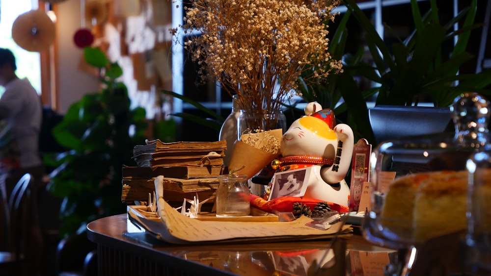 a small figurine on a table with a vase of flowers