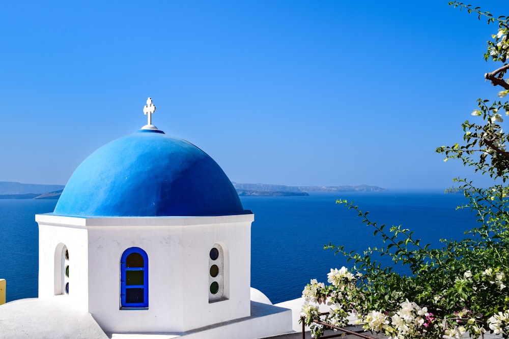 a white building with a blue dome and a cross on top by water