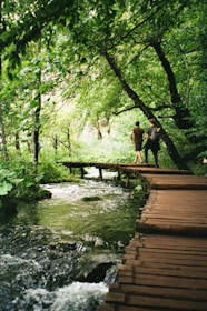 a group of people walking on a wooden bridge over a river