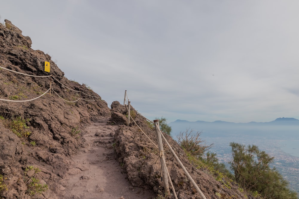 a path with a fence and a hill with a body of water in the background