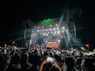 A group of friends smiling and taking a selfie with the festival stage glowing behind them.