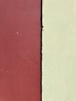 Two adjacent walls of contrasting colors are visible, one in a deep maroon red and the other in a pale yellow-green. The textures of the walls suggest a rough, painted surface, and they are separated by a vertical line where the two colors meet.