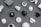 A variety of smart home devices are arranged on a flat surface, including sensors, plugs, and hubs. The devices are mostly black and white, with some showing LED indicators and branding. The background is a muted gray, emphasizing the sleek and modern design of the gadgets.