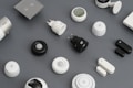 A variety of smart home devices are arranged on a flat surface, including sensors, plugs, and hubs. The devices are mostly black and white, with some showing LED indicators and branding. The background is a muted gray, emphasizing the sleek and modern design of the gadgets.