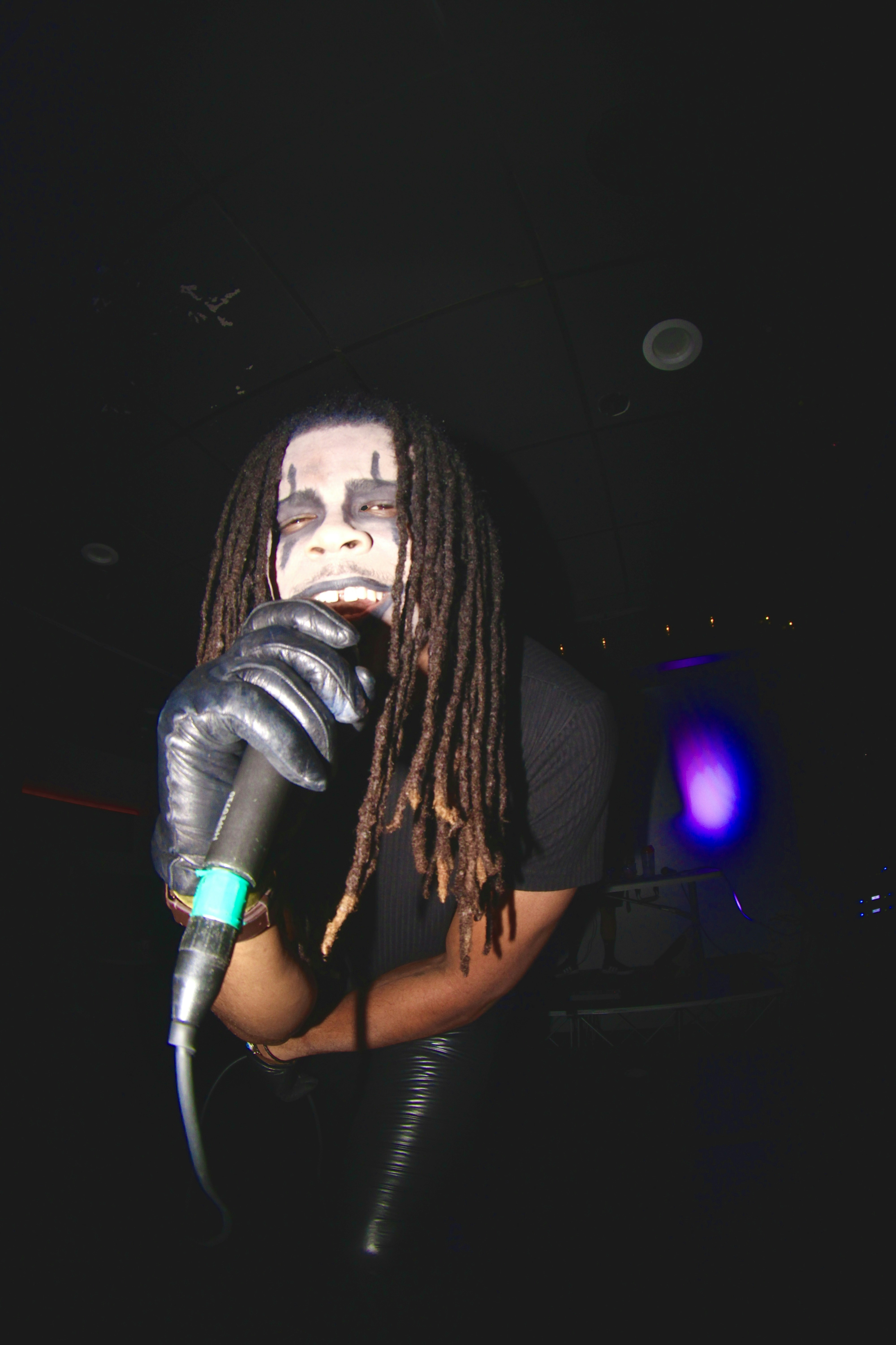 Male reggae musician with long thick dreadlocks performing outdoors, dramatic low-key lighting, deep shadows, moody dark background