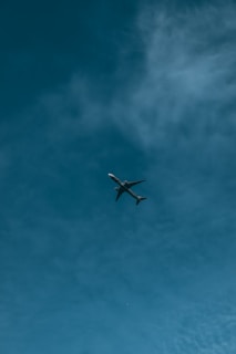 An orange passenger plane soaring above fluffy white clouds under a clear blue sky.
