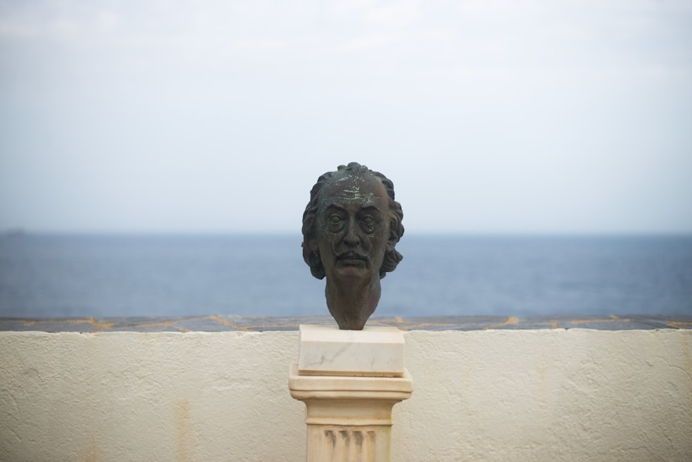 a statue of a head on a pedestal by the water