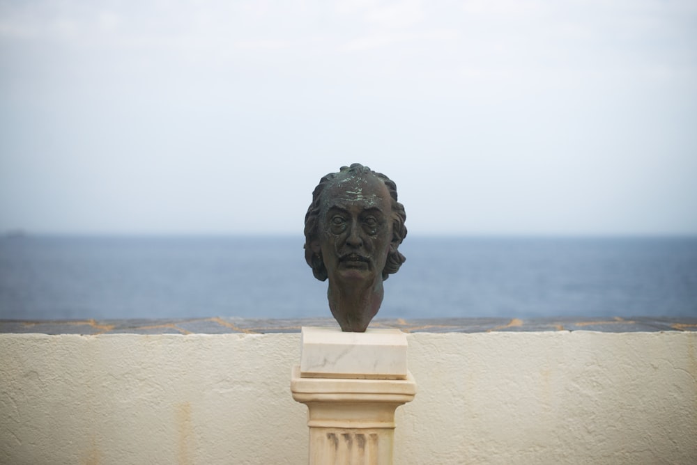 Una estatua de una cabeza en un pedestal junto al agua