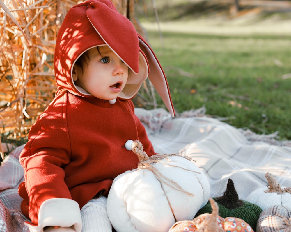 a baby in a red hoodie and red hat sitting in the grass
