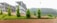 A landscape featuring a series of small, well-maintained shrubs and plants arranged on a grassy slope with carved shapes. In the background, there is a multi-storey concrete building under construction, and the setting is bordered by a lush forested hill.