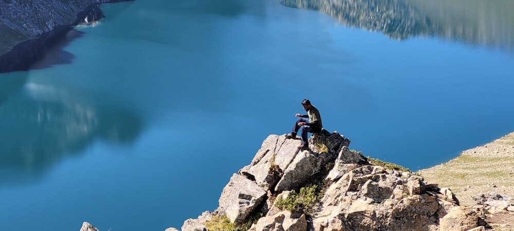 a person sitting on a rock by a body of water