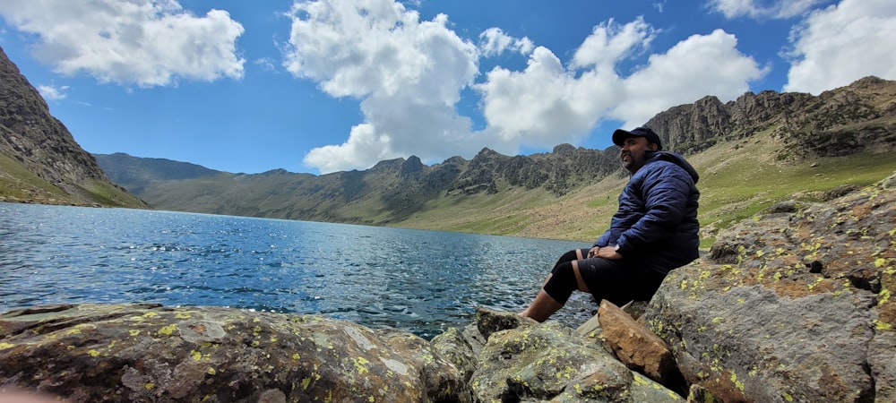 a man sitting on a rock by a body of water