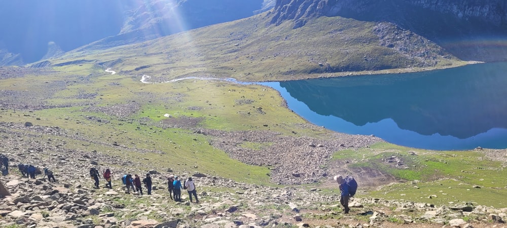 a group of people walking on a rocky path by a lake