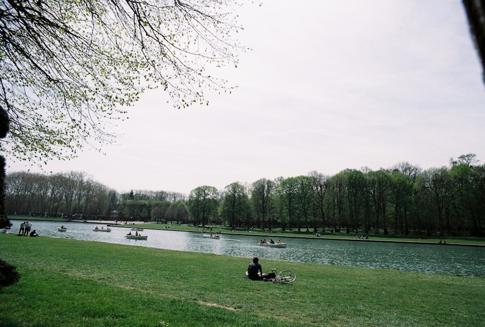 a person sitting on a blanket by a lake with boats on it