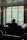 A thoughtful man seated in a cozy room, looking out a window with a hopeful expression.