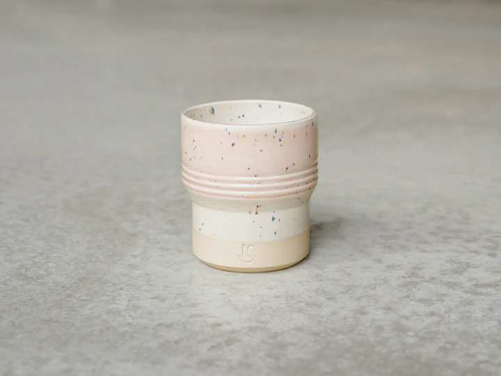 Speckled cream stoneware mug on grey concrete — soft Shino-style glaze