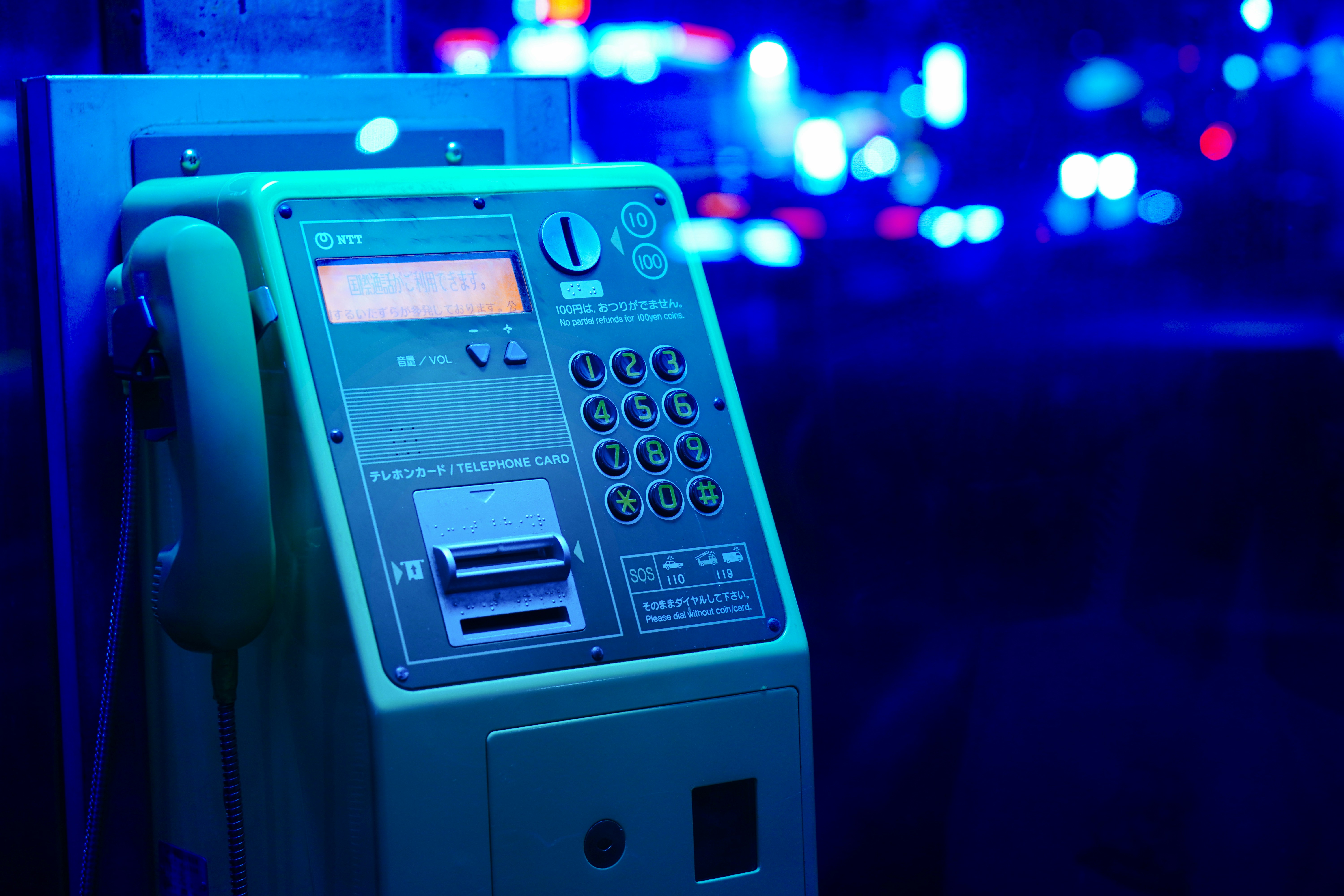 Telephone card payphone illuminated in blue light, showcasing keypad and display, relevant to discussions on digital fraud detection and security measures.