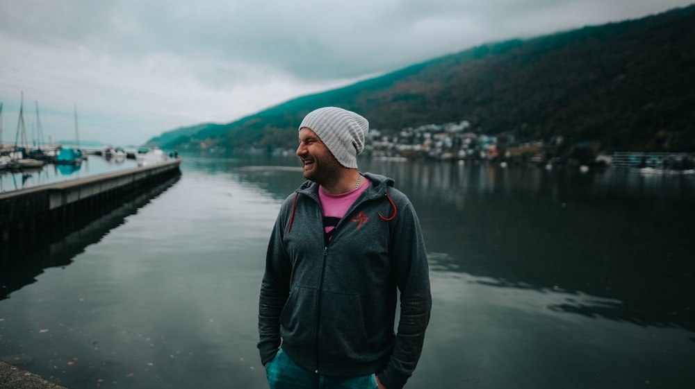 a man standing in front of a body of water with boats and hills in the background