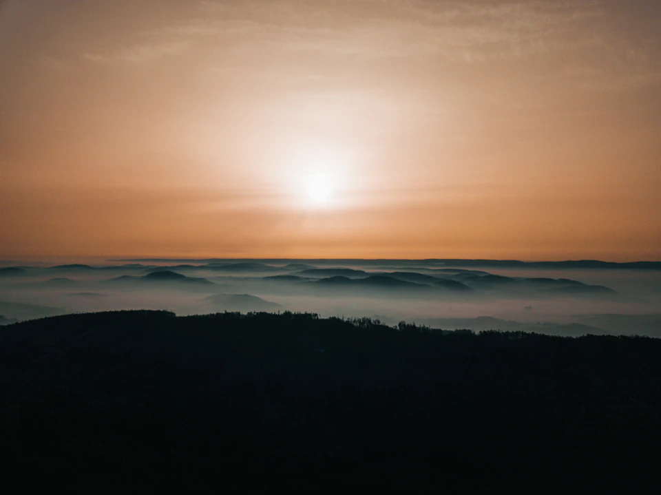 Sunrise over foggy mountain range with warm glow and soft light illuminating the scene