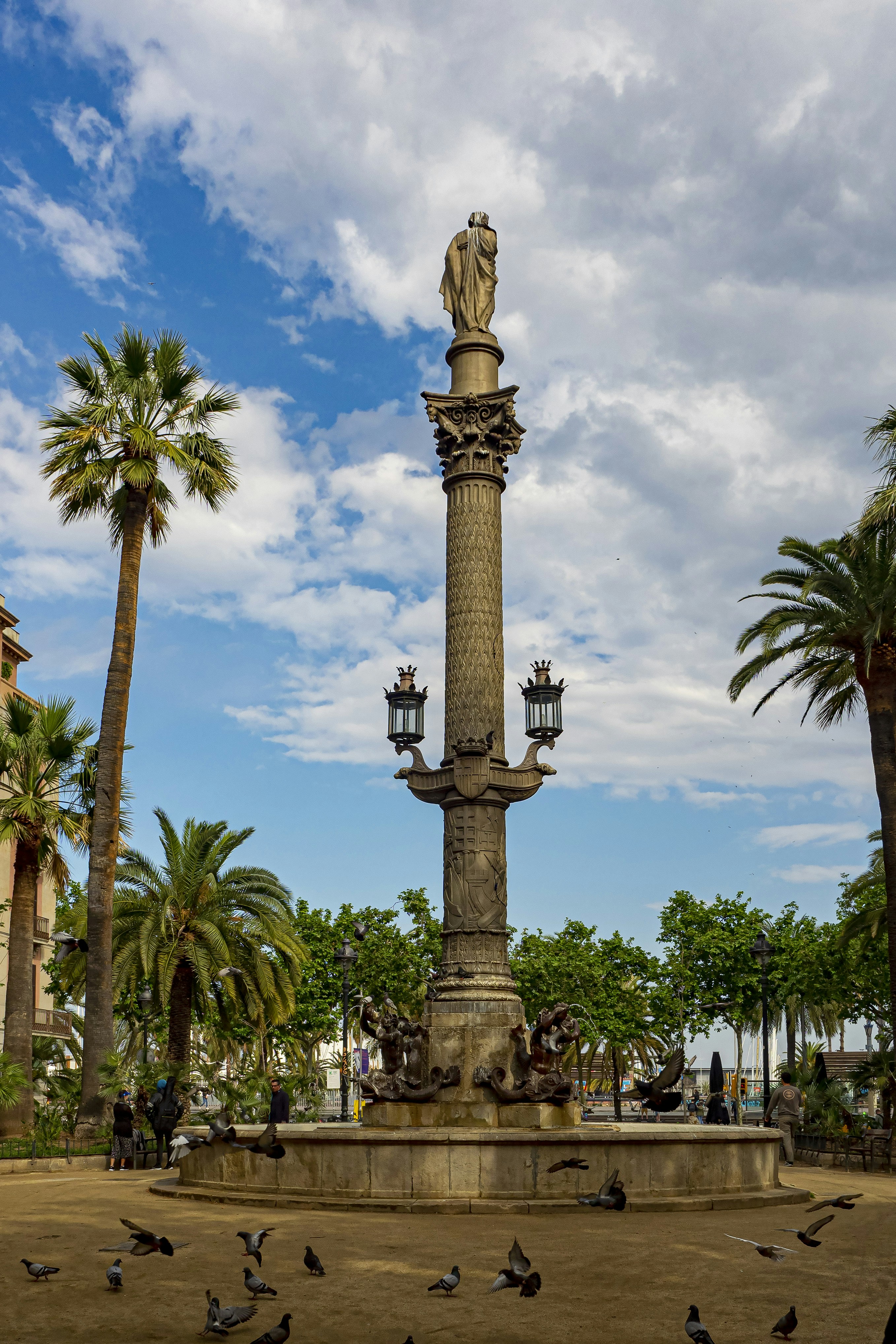 a tall statue with a gold top surrounded by trees and people