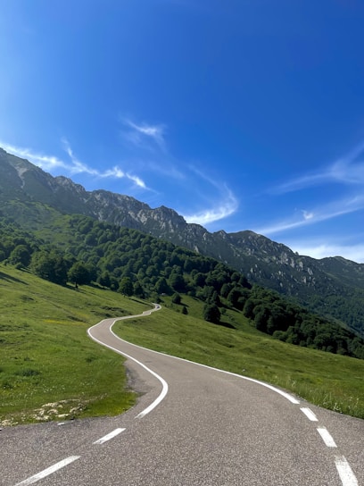 A winding road through lush green mountains with a clear blue sky.