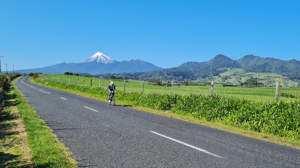 a person riding a bicycle on a road with mountains in the background