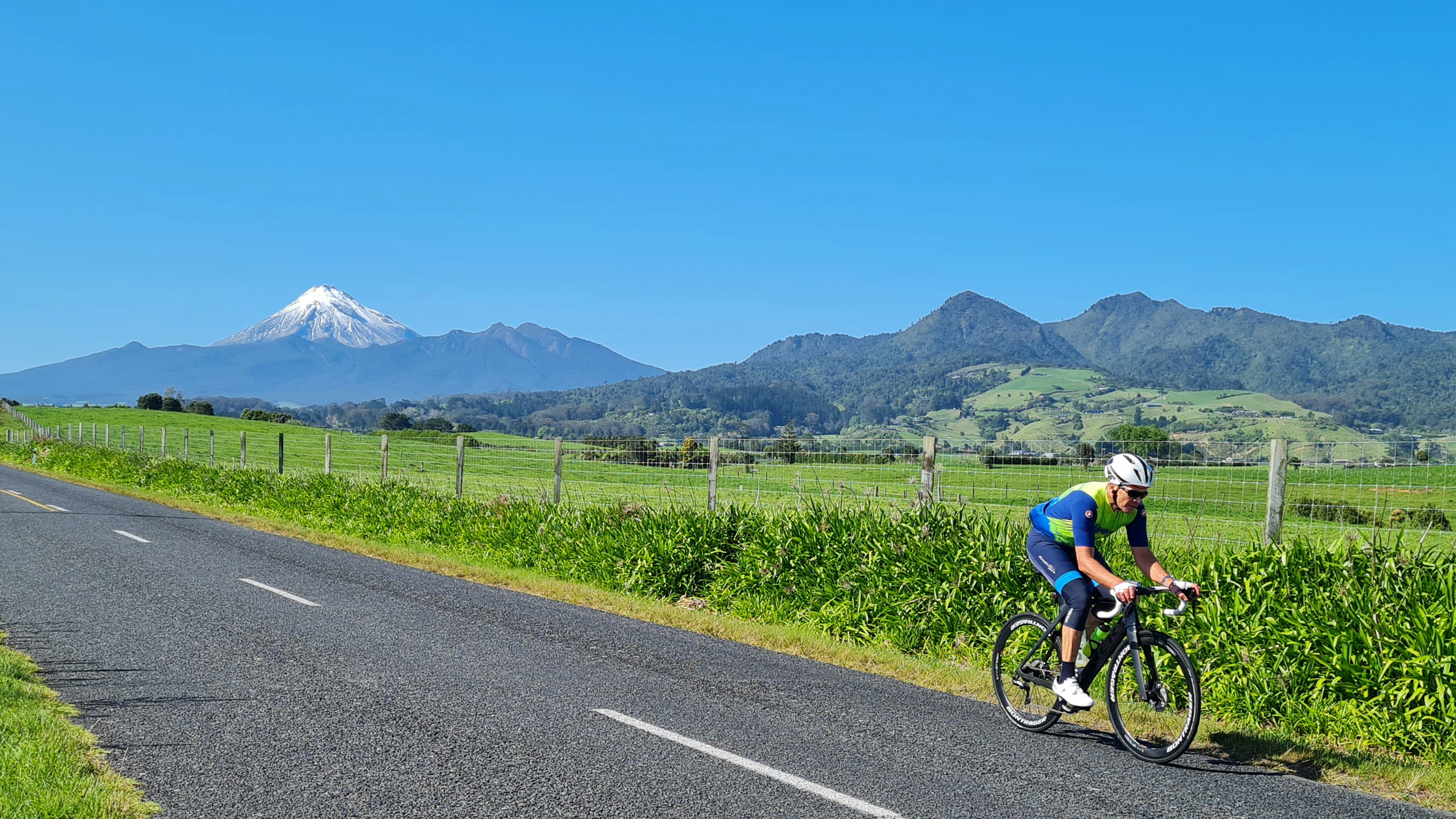 a person riding a bicycle on a road with grass and mountains in the background