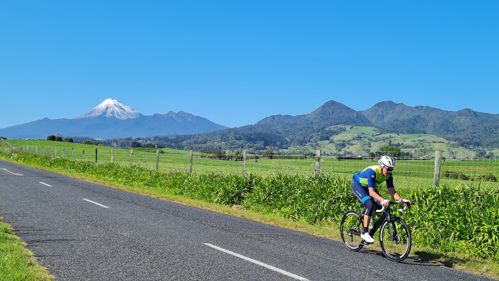 a person riding a bicycle on a road with grass and mountains in the background