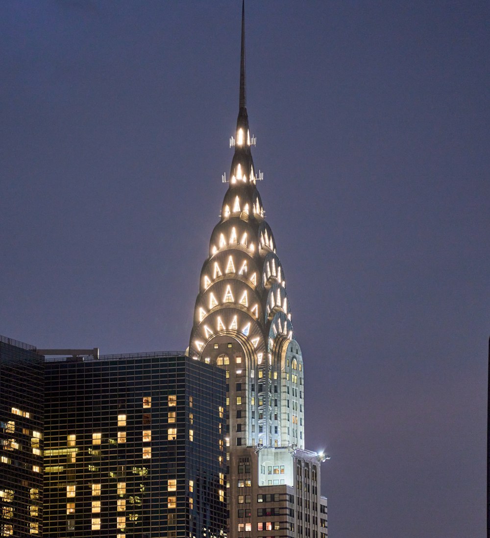 a tall building with lights at night with Chrysler Building in the background