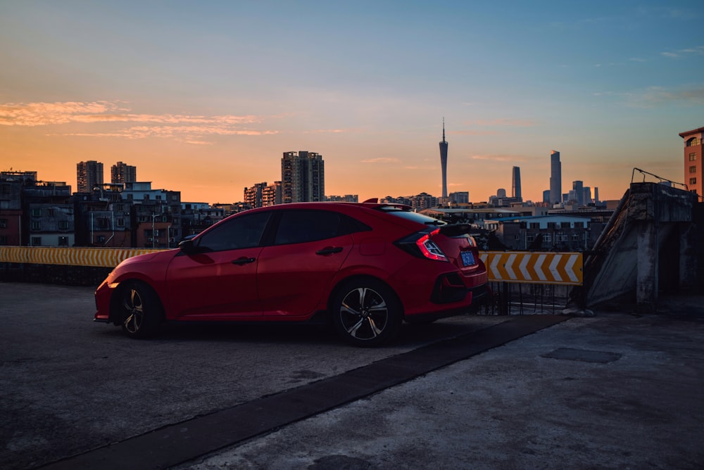 a red car parked on a road with a city skyline in the background