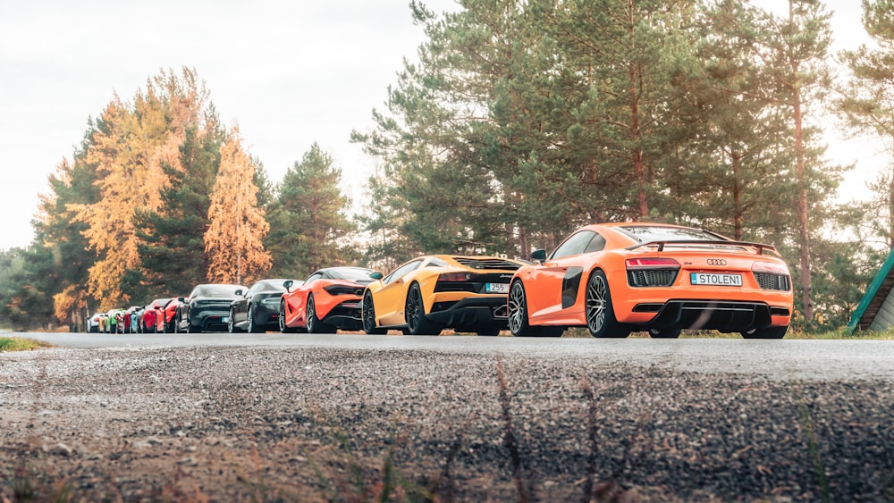 a row of sports cars parked on a road with trees in the background