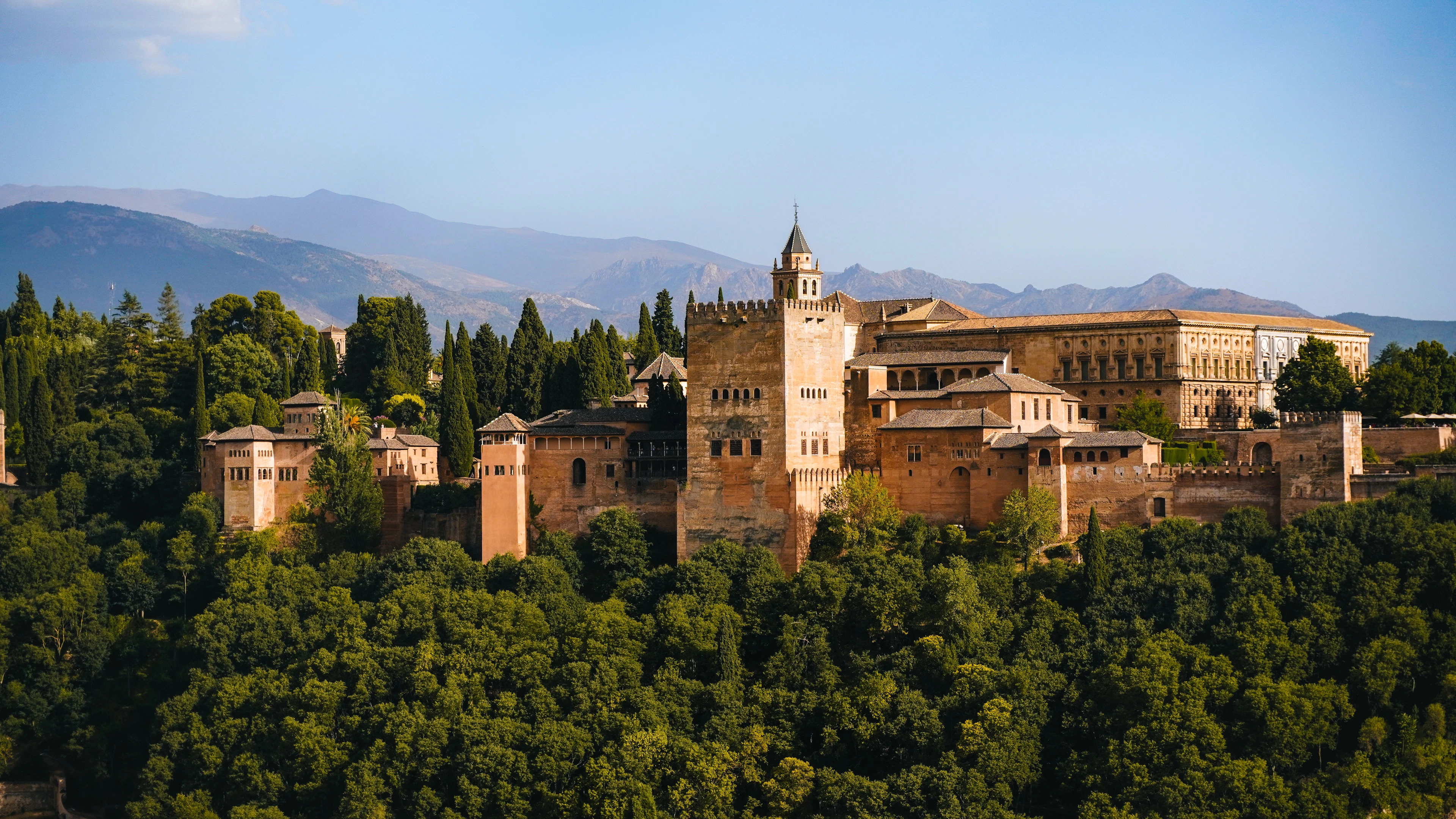 The fortress towers and palaces of the Alhambra in Granada glowing in warm evening light above a sea of green trees