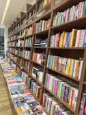 Rows of books neatly arranged on wooden shelves, featuring sections labeled nonfiction and classics. A long table displays various books lying flat, showcasing their covers.