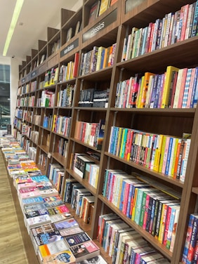 Rows of books neatly arranged on wooden shelves, featuring sections labeled nonfiction and classics. A long table displays various books lying flat, showcasing their covers.