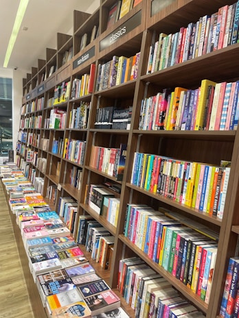 Rows of books neatly arranged on wooden shelves, featuring sections labeled nonfiction and classics. A long table displays various books lying flat, showcasing their covers.