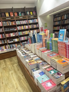 A bookstore with neatly arranged books on wooden shelves and several tables. The shelves are labeled with categories such as classics and fiction. Brightly colored book covers add a vibrant touch to the scene.