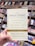A hand is holding a book titled 'The Daily Stoic' in front of a bookshelf filled with various books. The book cover mentions 366 meditations on wisdom, perseverance, and the art of living, featuring new translations of Seneca, Epictetus, and Marcus Aurelius. The authors are Ryan Holiday and Stephen Hanselman. The surrounding bookshelf sections are labeled with categories such as lifestyle and children's.
