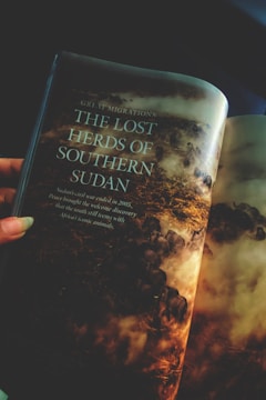 A page from a magazine displays a vivid image of a herd of animals migrating through a dusty landscape, accompanied by a text about the 'Lost Herds of Southern Sudan'. The page is slightly curved, suggesting it is part of a bound magazine.