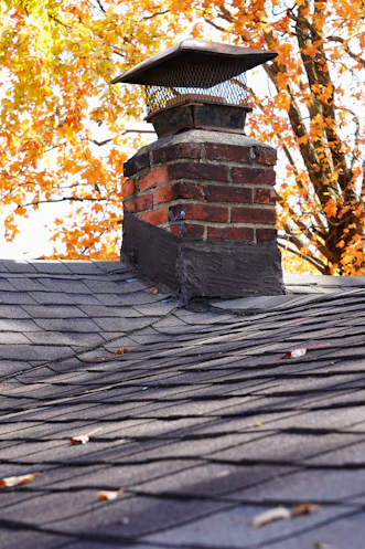 A friendly chimney sweep carefully cleaning a chimney on a cozy home in Torrington, with autumn leaves around.
