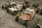 Several vintage-style toy cars are neatly arranged on a paved surface. The cars are colorful with chrome accents, wooden frames, and intricate detailing, each featuring a steering wheel and cushioned seat.