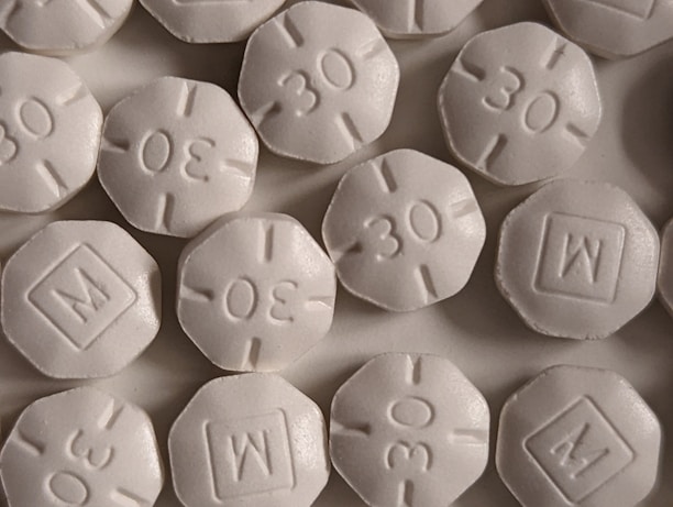 A close-up view of several round, white pills with an embossed '30' and 'M' in a square on them. The pills are arranged closely, partially overlapping.