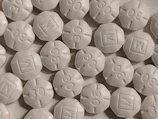 A close-up view of numerous white, round, tablet-like pills with markings '30' and 'M' embossed on them. The pills are arranged in a scattered pattern filling the entire frame.